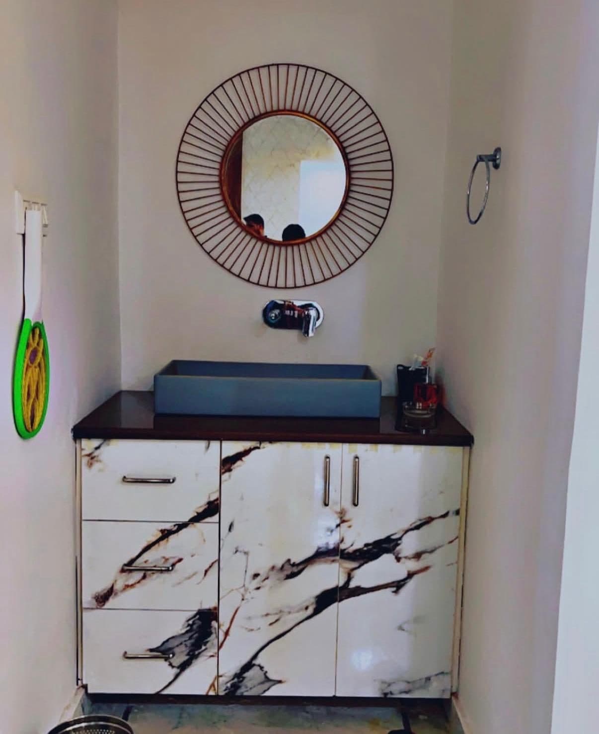 Bathroom vanity with marble-finish laminate cabinets, wooden counter, basin and round rattan mirror